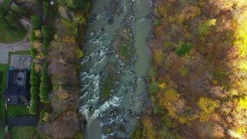 a zangão movimentos baixa sobre a outono floresta e a rio e a casa próximo. aéreo Visão do floresta e montanha rio com colorida folhas em árvores, topo visualizar. topo Visão do outono árvores video