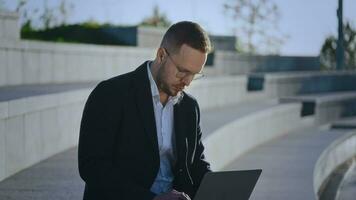 een elegant mannetje manager is werken Aan een laptop buiten de kantoor. mooi zo weer staat toe u naar werk buiten, van een afstand video