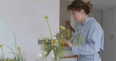 vrouw aan het doen nieuw boeket. meisje werken in bloem winkel studio. vrouw bloemist artiest reinigt bloemen voor een mooi boeket, werkplaats visie. video