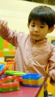 un pequeño asiático chico es jugando con un cuadrado magnético rompecabezas. video