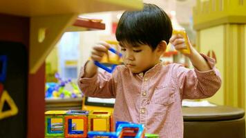 A little Asian boy is playing with a square magnetic puzzle. video