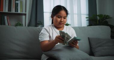 Portrait of young Asian woman enjoy counting cash dollars banknotes on sofa in the living room at home. photo