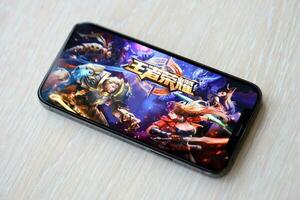 Honor of Kings mobile iOS game on iPhone 15 smartphone screen on wooden table during mobile gameplay photo
