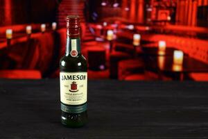 KHARKOV, UKRAINE - FEBRUARY 14, 2021 Jameson triple distilled irish whiskey bottle on wooden table with red bar interior on background. Elite alcohol photo