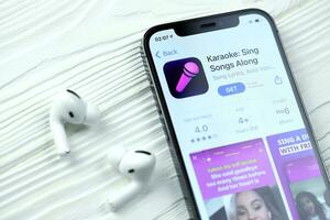 KHARKOV, UKRAINE - MARCH 5, 2021 Karaoke icon and application from App store on iPhone 12 pro display screen with airpods pro on white table photo