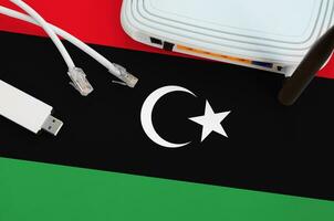 Libya flag depicted on table with internet rj45 cable, wireless usb wifi adapter and router. Internet connection concept photo