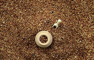 Background image of a large pile of buckwheat, in the middle of which lies a small jug and a wooden spatula for cereals photo