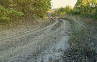 Autumn landscape with a curved road and traces of the tread of large wheels of agricultural machinery photo