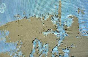 The texture of the wall, covered with gray foam polystyrene plates, covered with a blue reinforcing mesh and covered with a mixture for gluing it. Stage of wall insulation photo