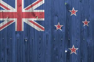 nuevo Zelanda bandera representado en brillante pintar colores en antiguo de madera pared. texturizado bandera en áspero antecedentes foto