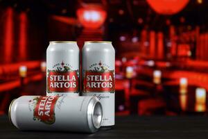 KHARKOV, UKRAINE - FEBRUARY 14, 2021 Stella Artois beer cans on wooden table with red bar interior on background photo