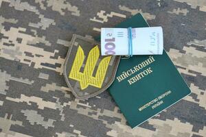 Symbol of Ukrainian army and military ID with bunch of money on the camouflage uniform of a Ukrainian soldier. Concept of payment to military personnel or bribe for deferment from service photo