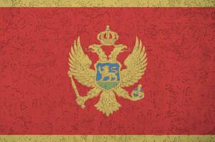 Montenegro flag depicted in bright paint colors on old relief plastering wall. Textured banner on rough background photo