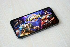 Honor of Kings mobile iOS game on iPhone 15 smartphone screen on wooden table during mobile gameplay photo