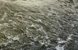 Waves of water of the river and the sea meet each other during high tide and low tide. Deep blue stormy sea water surface with white foam and waves pattern, background photo