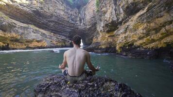 natureza amante jovem homem meditando dentro beira-mar caverna. video