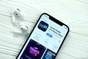 KHARKOV, UKRAINE - MARCH 5, 2021 TuneIn music icon and application from App store on iPhone 12 pro display screen with airpods pro on white table photo