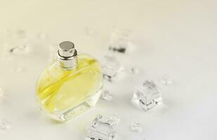 frasco amarillo de perfume femenino, fotografía objetiva del frasco de perfume en cubitos de hielo y agua sobre una mesa blanca. vista desde arriba. foto de producto de maqueta, concepto de frescura