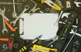 Handyman tool kit on black wooden table with copy space in blank paper tablet. Many wrenches and screwdrivers, pilers and other tools for any types of repair or construction works photo