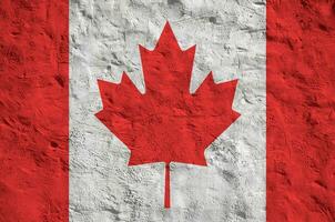 Canada flag depicted in bright paint colors on old relief plastering wall. Textured banner on rough background photo