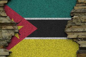 Mozambique flag depicted in paint colors on old stone wall closeup. Textured banner on rock wall background photo
