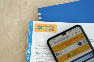 KYIV, UKRAINE - 4 MAY, 2023 Synevo medical analysis results and smartphone with synevo official website on screen photo