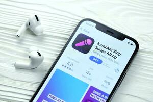 KHARKOV, UKRAINE - MARCH 5, 2021 Karaoke icon and application from App store on iPhone 12 pro display screen with airpods pro on white table photo