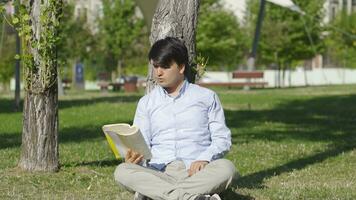 jovem homem lendo uma livro dentro a parque. video