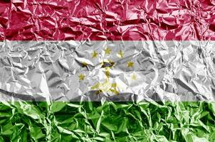 Tajikistan flag depicted in paint colors on shiny crumpled aluminium foil closeup. Textured banner on rough background photo