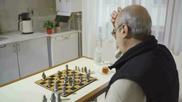 Happy and cheerful old man playing chess by himself. video