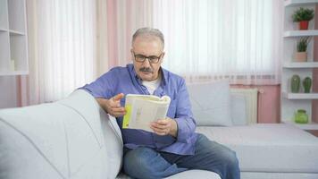 a mal humorado velho homem pega Bravo às a livro ele é leitura. video