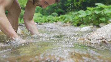Sporty teenager washing face at the creek. Slow motion. video