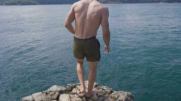 Mann springt in Wasser von das Felsen Neigung. Sommer- Spaß Lebensstil. video