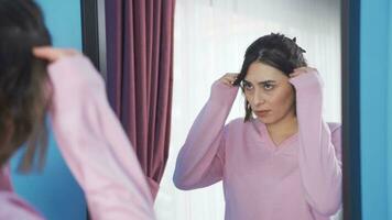 Unhappy young woman looking at her hair in the mirror. video