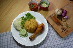 Brown Arabian biryani comes with chicken thighs and various sides, including ajhab, vegetables, sauce, spices, garlic, shallots, all on a cutting board. photo