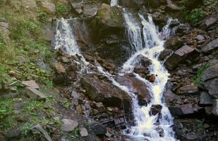 A mountain waterfall flows over the rocks. Waterfall cascade on mossy rocks photo