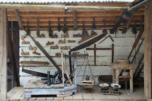 Collection of planers and retro wood saws hang on a wooden wall near an old house. Carpenters plane and other things on wall photo