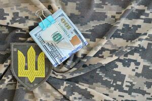 Ukrainian army symbol and bunch of dollar bills on military uniform. Payments to soldiers of the Ukrainian army from United States, salaries to the military. War support photo