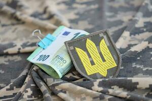 Ukrainian army symbol and bunch of euro bills on military uniform. Payments to soldiers of the Ukrainian army from European union, salaries to the military. War support photo