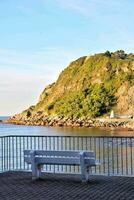 a bench overlooking the ocean and a hill photo