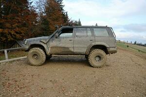 Automobile in a countryside landscape with a mud road. Off-road 4x4 suv automobile with ditry body after drive in muddy road photo