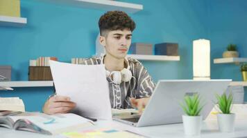 Student looking at document in hand and taking notes on laptop. Homework. video