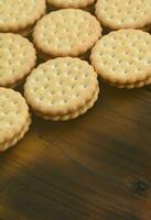 A round sandwich cookie with coconut filling lies in large quantities on a brown wooden surface. Photo of edible treats on a wooden background with copy space