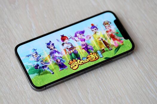Fantasy Westward Journey mobile iOS game on iPhone 15 smartphone screen on wooden table during mobile gameplay photo