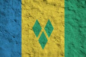 Saint Vincent and the Grenadines flag depicted in bright paint colors on old relief plastering wall. Textured banner on rough background photo