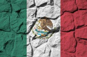 Mexico flag depicted in paint colors on old stone wall closeup. Textured banner on rock wall background photo