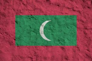 Maldives flag depicted in bright paint colors on old relief plastering wall. Textured banner on rough background photo