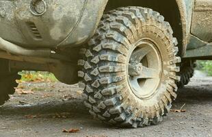 Wheel closeup in a countryside landscape with a mud road. Off-road 4x4 suv automobile with ditry body after drive in muddy road photo