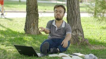 un Universidad enano estudiante estudiando al aire libre en el parque es olvidadizo. video