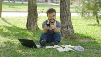 Phone addicted young college dwarf student doing homework outdoors. video